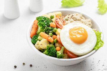 Savory oatmeal bowl with fried egg and steamed vegetables. Space for text.