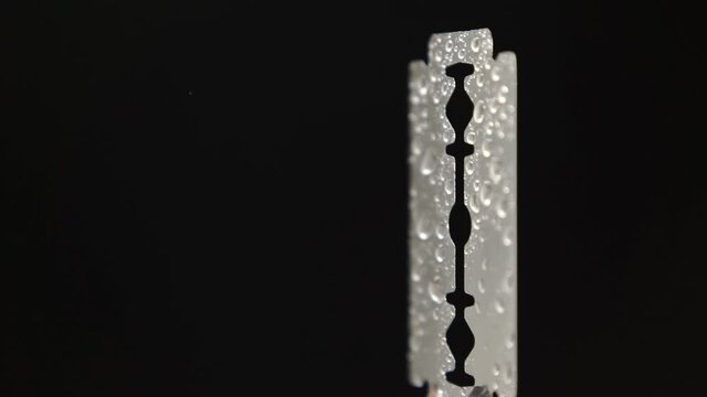 Traditional razor blade with water droplets on black background. Macro shooting. Rotation