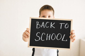 Boy with backpack holding in his hands chalk board with inscription Back to school isolated on white background