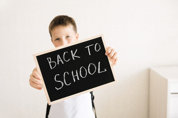 Boy with backpack holding in his hands chalk board with inscription Back to school isolated on white background