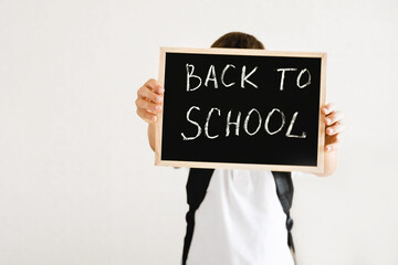 Boy with backpack holding in his hands chalk board with inscription Back to school isolated on white background