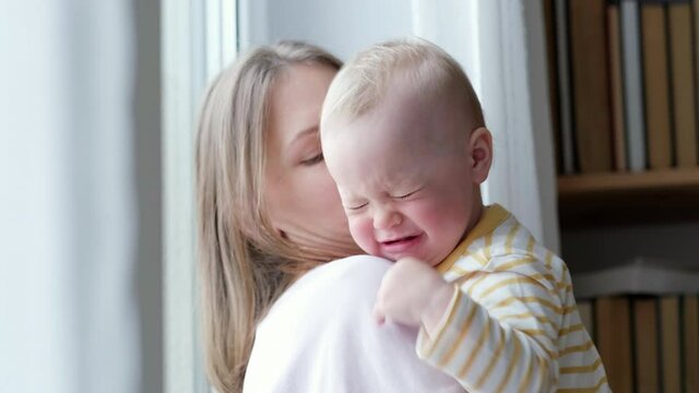 Mom hugging and soothing her crying baby Little infant child crying looking in camera on mother hand. Family love