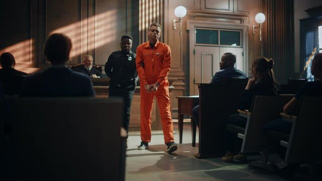 Cinematic Court of Law and Justice Trial Proceedings: Portrait of Accused Sad Male Criminal in Orange Jumpsuit Led Away by Security Guard in Front of Judge and Jury. Sentenced to Serve Jail Time.