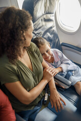 High angle view of little girl sitting on the plane, leaning on her mother while traveling together. Family, vacation concept