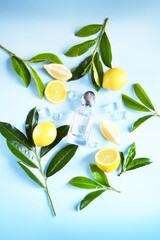 Glass transparent bottle of perfume with yellow lemons, ice cube, water drops and green tree branches on the blue background. Fresh summer unisex smell. Cooling citrus aroma.  
Perfume for hot weather