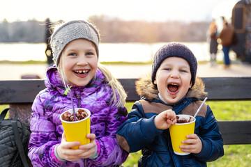 Two cute adorable siblings children sitting on bench drink delicious yummy hot chocolate, tea cocoa...