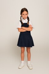 full length view of offended schoolchild standing with crossed arms on grey