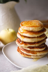 Stack of apple pancakes with pouring honey on white plate
