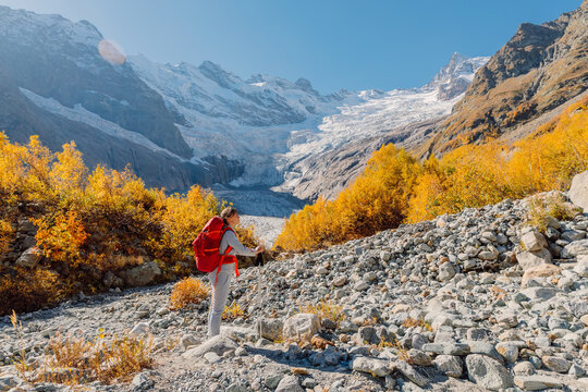 Hiker woman with backpack in autumnal mountains. Mountain with glacier and hiker