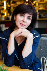 A dreaming brunette woman is sitting at a table in cafe waiting for her food.