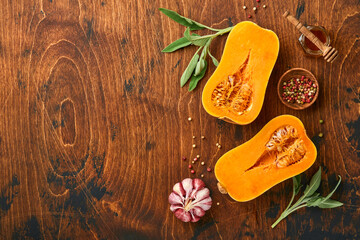Halves of raw organic butternut squash with sage leaf, multicolored pepper garlic, honey, salt and pepper on old wooden background. Food background. Top view with copy space.