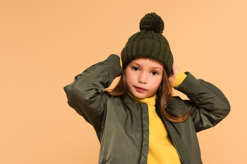 kid in brown hat and jacket posing with hands behind head isolated on beige