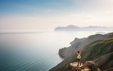Young man travels alone on the backdrop of the mountains standing on top of a mountain with raised...