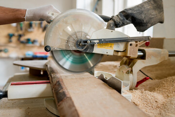 Close up of carpenter cutting with radial arm saw. Woodworker using electric jigsaw in workshop for production of wooden furniture. Joinery work concept.