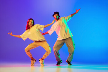 Two young people, guy and girl in casual clothes dancing contemporary dance, hip-hop over blue...