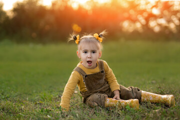 A little girl is sitting on the ground on an autumn evening at sunset with her mouth open with...