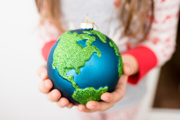 Close-up of little girl holding in hands Xmas glass bauble decoration ornament globe planet earth....