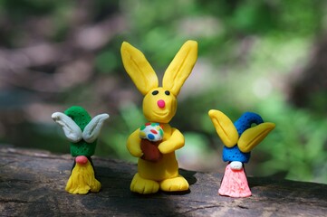Figures of Easter gnomes with ears made of plasticine and a rabbit on a colored background.