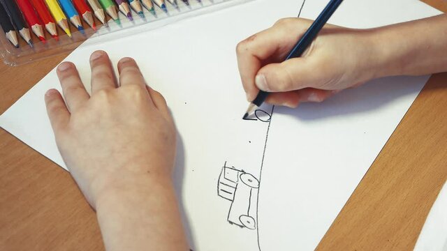 Children's hand draws cars on the road with a colored pencil. Leisure of a happy child, quarantine, isolation. The concept of children's creativity, online education. Top view, flat lay. UHD 4K.