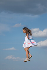 A beautiful little girl in a white dress is jumping on the background of the sky.