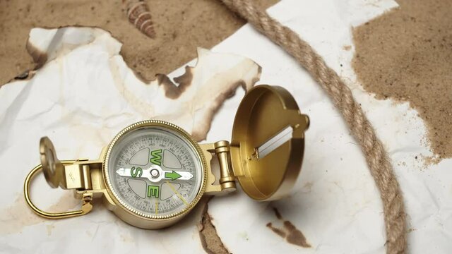 Man hand putting gold compass on burnt maps on sand background close-up, golden compass in human palm. Traveling and tourism concept, navigation.