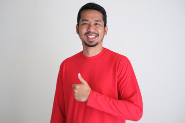 Adult Asian man wearing red clothes smiling happy and giving thumb up