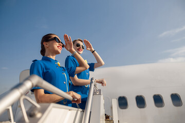 Portrait of two elegant air stewardesses in blue uniform and sunglasses covering eyes with hand and...