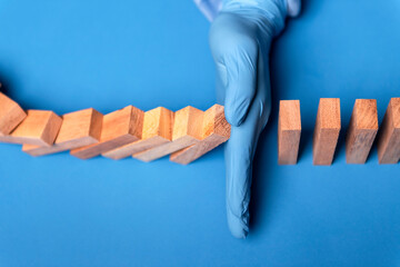 hand of doctor in medical glove stopping falling domino in a virus crisis management concept image.