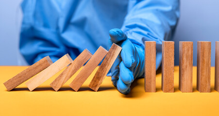 hand of doctor in medical glove stopping falling domino in a virus crisis management concept image.