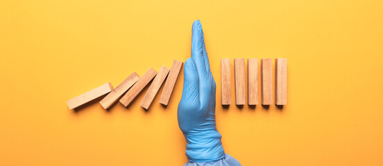 Doctor wearing protective equipment (PPE), hand of doctor in medical glove stopping falling domino...