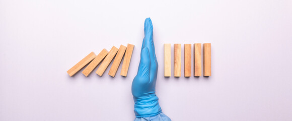 hand of doctor in medical glove stopping falling domino in a virus crisis management concept image.