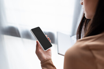partial view of woman holding mobile phone with blank screen.
