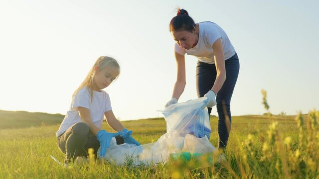 Mom and daughter cleaning plastic waste. Mother with her daughter collecting garbage on a meadow next to the river.
