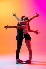 Two dancers, stylish sportive couple, male and female models dancing contemporary dance on colorful gradient yellow pink background in neon light.