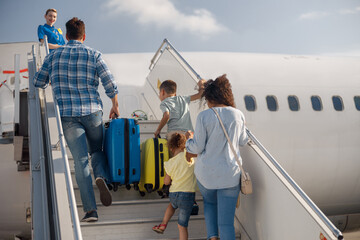 Back view of family of four getting on, boarding the plane on a daytime, ready for summer vacations. People, traveling, vacation concept © Yaroslav Astakhov