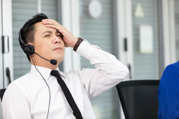 male operator wearing headphones, feeling tired and have a headache form overworked at call center...