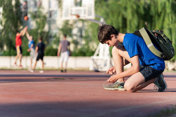 a guy ties his shoelaces on the edge of the field, next to the team playing basketball