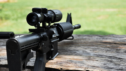 Black automatic rifle Long-barreled which has binoculars on wooden table at the training ground, also known as Air Soft or BB Gun, soft and selective focus on gun.
