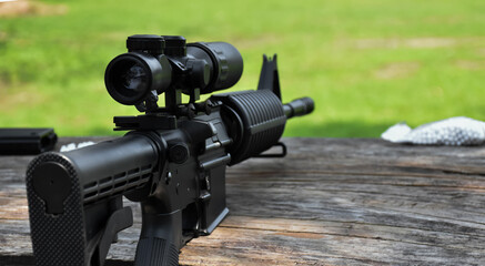 Black automatic rifle Long-barreled which has binoculars on wooden table at the training ground, also known as Air Soft or BB Gun, soft and selective focus on gun.