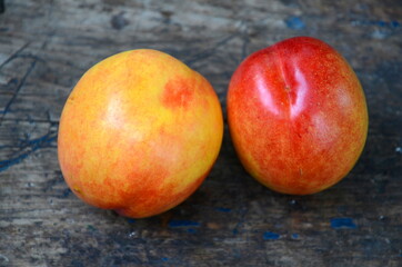 Two ripe juicy fruits of nectarine lie on a wooden surface.