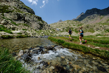 Fototapeta na wymiar couple of mountain runners next to a river, Ibones azules and Bachimaña alto route, Huesca province, Spain
