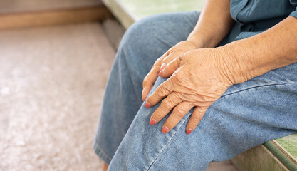 Close up shot of 80 years old woman sitting and touching her knees with hands due to feeling pain...