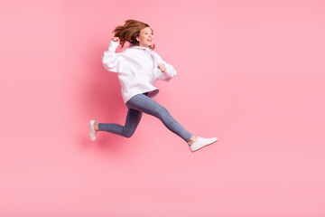 Fototapeta na wymiar Photo of sweet shiny school girl wear white hoodie smiling jumping high running looking empty space isolated pink color background