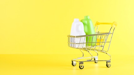 Shopping cart with bottles inside on a yellow background, closeup. Black Friday Shopping and Discount Concept