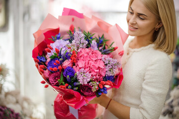 happy blonde woman holds beautiful bouquet of mixed flowers wrapped in bright pink paper