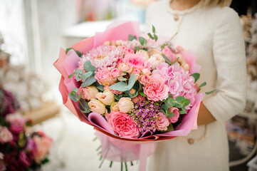 great bouquet of pink chrysanthemum hydrangea and roses wrapped in paper in woman hands.