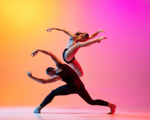 Fototapeta na wymiar Two dancers, stylish sportive couple, male and female models dancing contemporary dance on colorful gradient yellow pink background in neon light.