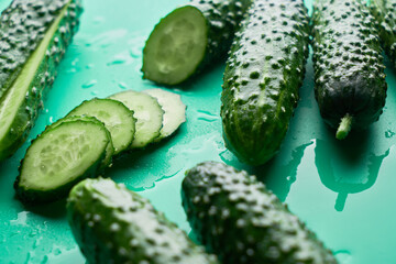 Set of fresh whole and sliced cucumbers on a green background with water drops. Garden cucumber wallpaper backdrop design