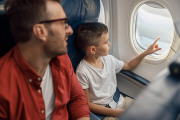 Curious little boy looking out the window while traveling by plane together with his father. Family, transportation, vacation concept © Yaroslav Astakhov