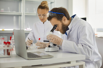 Male and female research scientists lab experts working with blood test sample and microscope checking result analyzing virus vaccine for treatment. Laboratory, medicine and healthcare